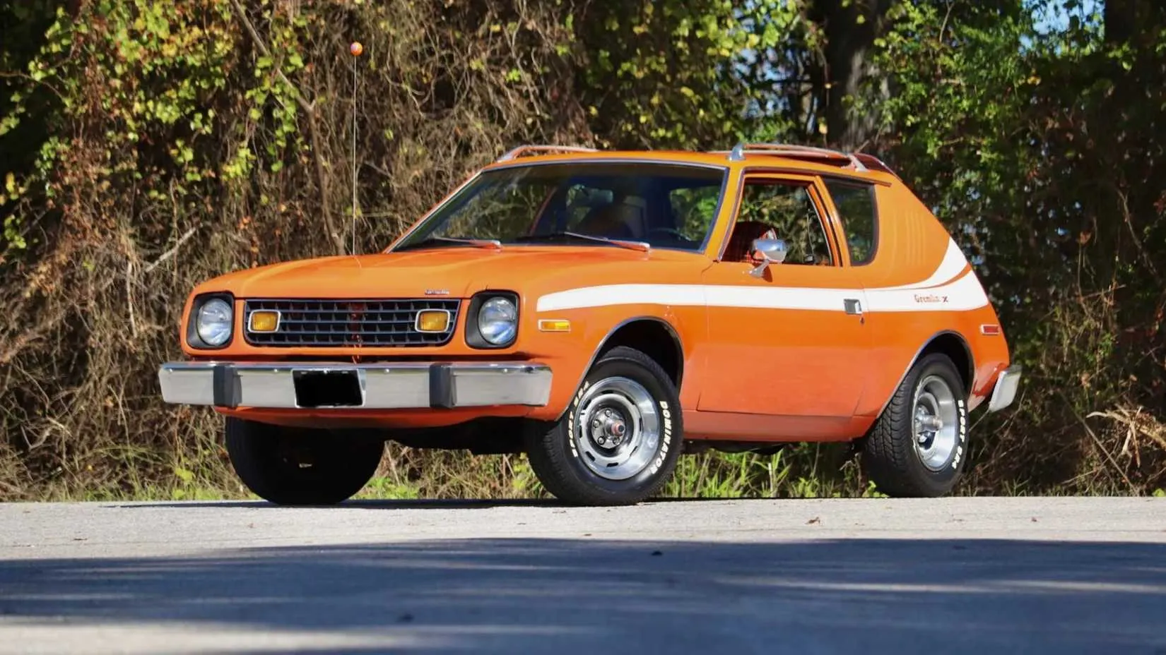 A rear three-quarter view of a 1977 AMC Gremlin X with a blacked-out grille and rally wheels
