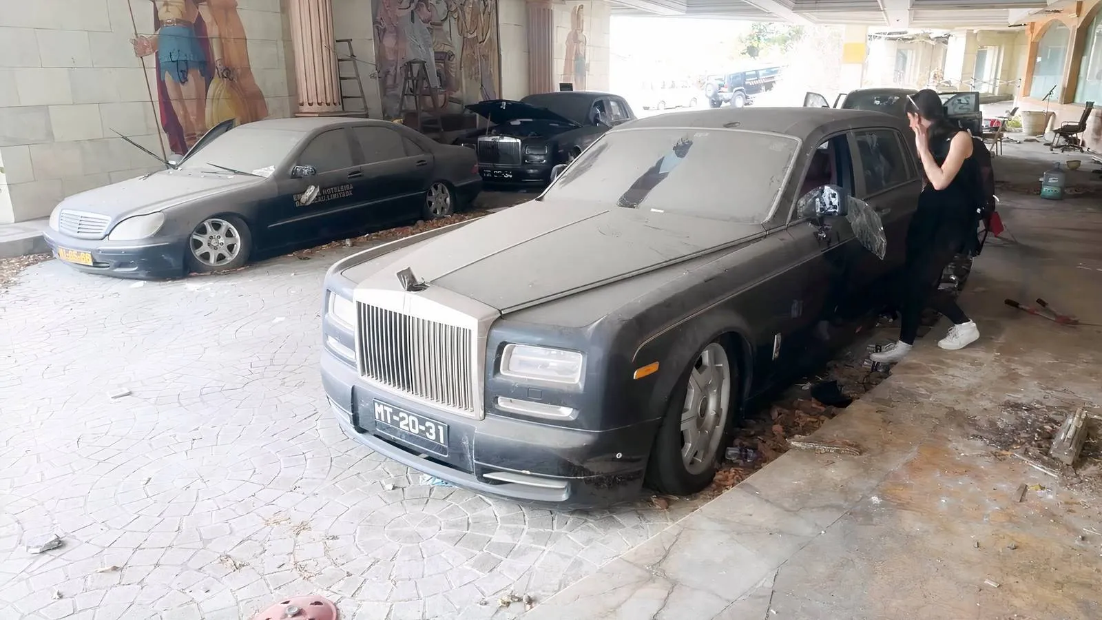 Three abandoned Rolls-Royce Phantoms at the hotel entrance, their dignified stance marred by vandalism and sagging suspensions.