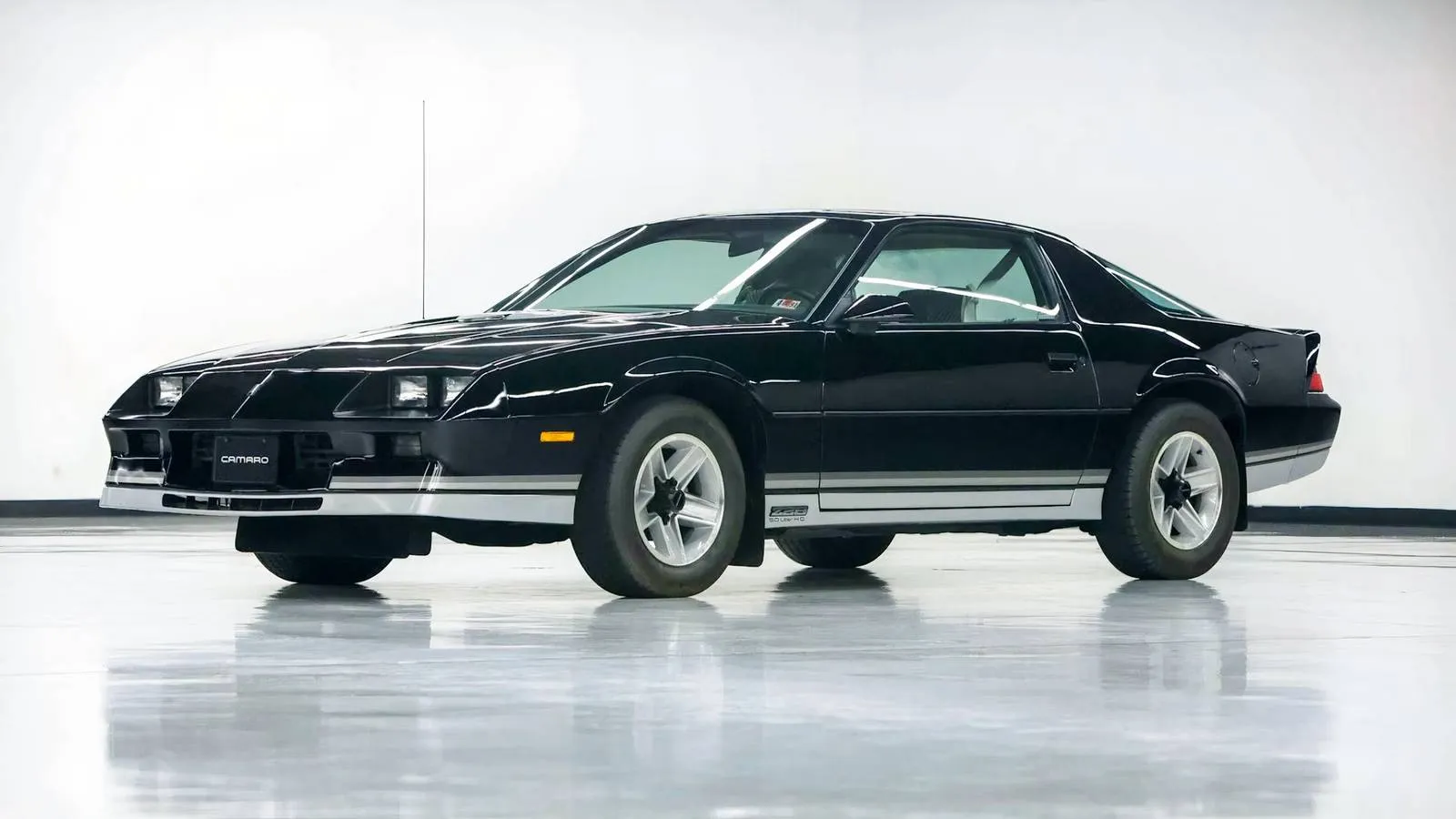 A pristine black 1984 Chevrolet Camaro Z28 with silver racing stripes, looking like it just rolled off the showroom floor