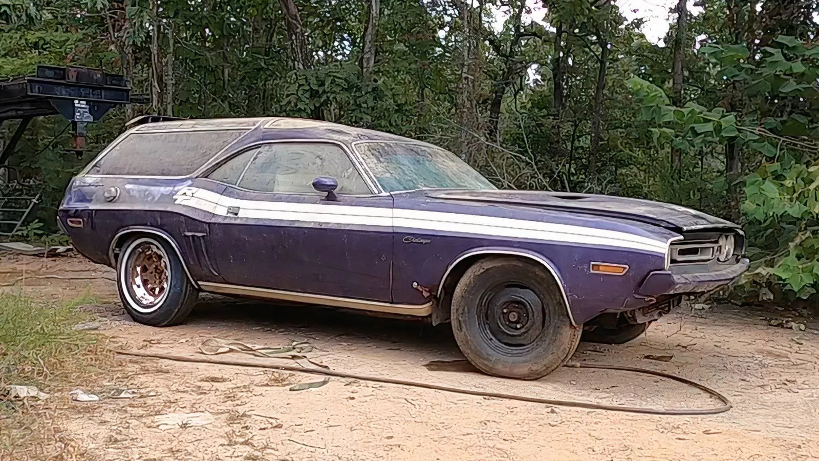 A 1971 Dodge Challenger R/T SE wagon conversion covered in thick dust, revealing its faded Plum Crazy paint and white stripes after a decade abandoned on a farm.