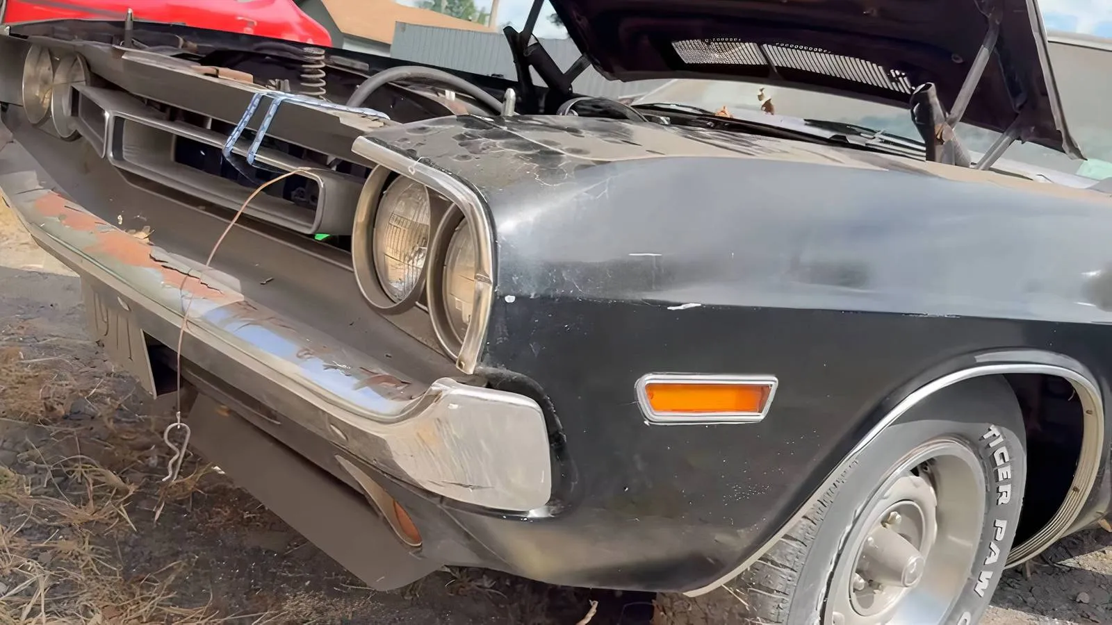 A weathered 1971 Dodge Challenger parked outdoors, showing its original TX9 Formal Black paint and classic muscle car stance
