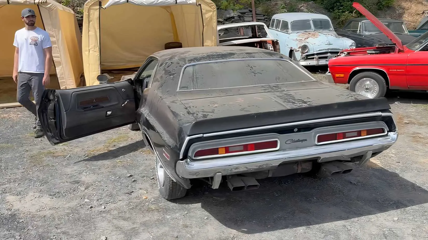 A black 1971 Dodge Challenger with visible wear, parked near other project cars